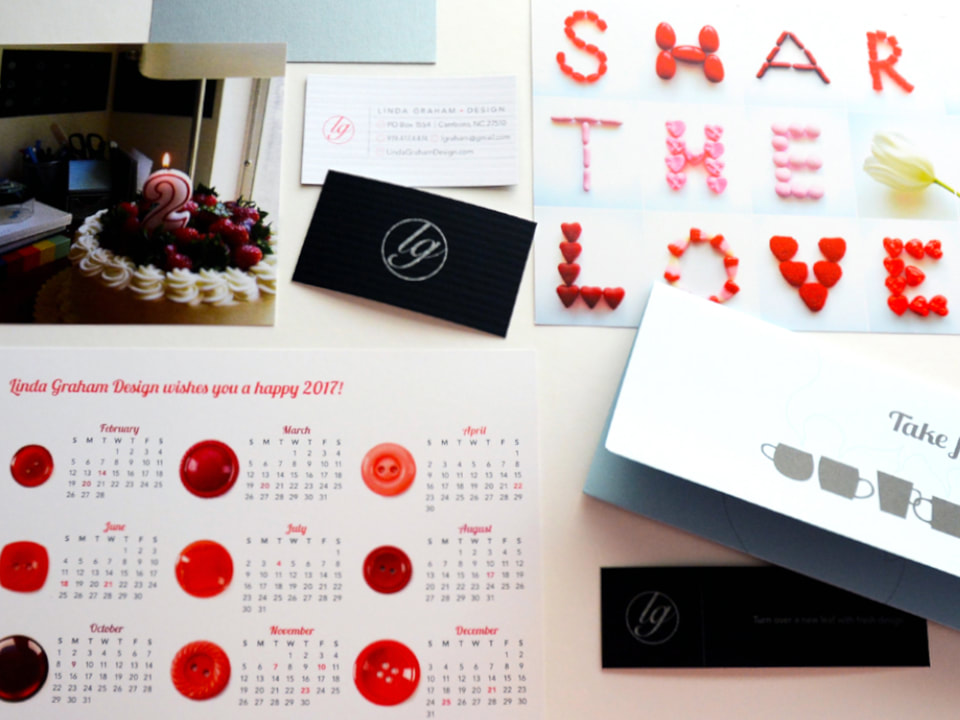 This photo shows a variety of Linda Graham Design printed materials, including a second business birthday card with a cake and candle, a calendar, a fifth anniversaty celebration with teas, business cards, a bookmark, and a Valentine’s charity donation postcard that spells out ‘Share the Love’ in red and pink candy.