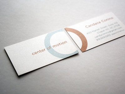 Close-up photograph of business cards with metallic copper and teal ink on a creamy, pearlescent paper. The logo shows the arc of a circle on one side continuing on the other. The font is a sans serif font.