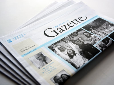 Photograph of a stack of folded University Gazette newspapers. The prominent photo is of a crowd cheering, focused on a girl with her arms up and her face up to the sky. The photography is black and white and the accent colors are light blue and pale yellow.