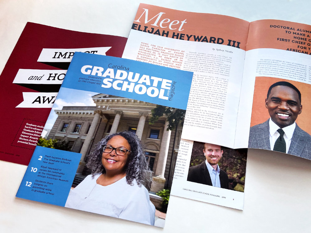 The cover of The Graduate school at UNC’s magazine has a Carolina blue banner across the top and rectangle in the lower left corner, with title and feature article text in white and black. The cover photo is a portrait of the school’s new dean, Suzanne Barbour, a Black woman with curly black and gray hair, black rectangular glasses, a white shirt, and a warm smile. To the left behind the cover you can see a maroon page with a white banner and black text. To the right behind the cover is an open spread with an orange bar across the top and text reading “Meet Elijah Heyward III and a photo of a smiling black man in a gray suit.
